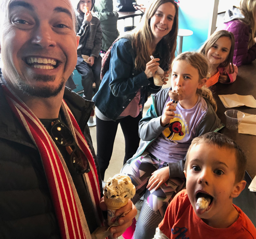 8 humans in photo. 6 facing camera with various types of ice cream and smiles.