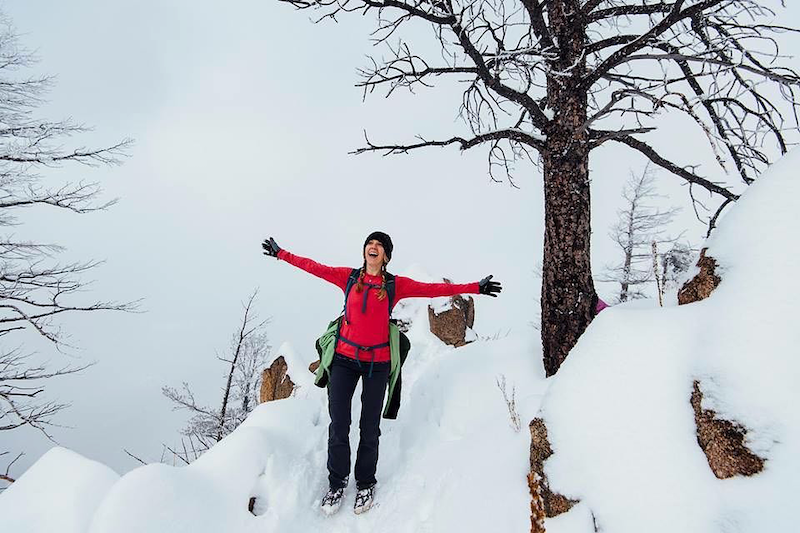 Human female wearing a pink shirt and dark pants, standing on a snowy trail in the mountains in Boulder, CO