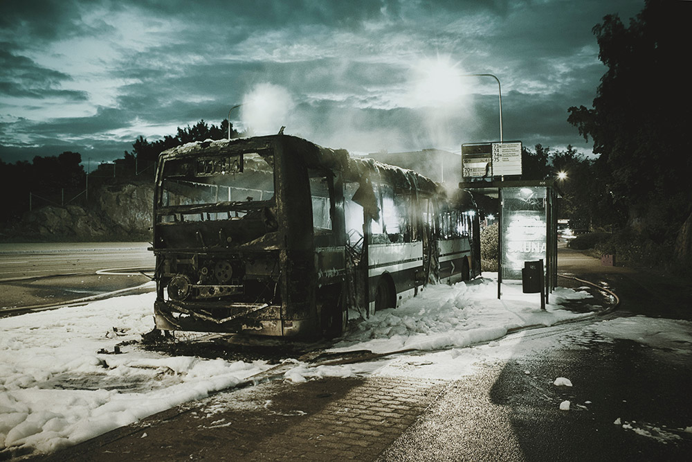 Bus that was on fire parked at bus stop with snow on the ground and clouds in the background.