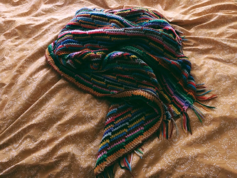 Multi-colored, crocheted blanket a top a yellow patterned duvet.