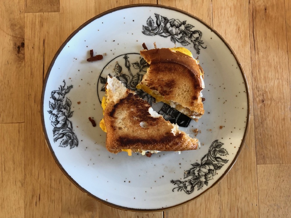 Photo of a grilled cheese sandwich with egg in the middle, on a plate, on a table.