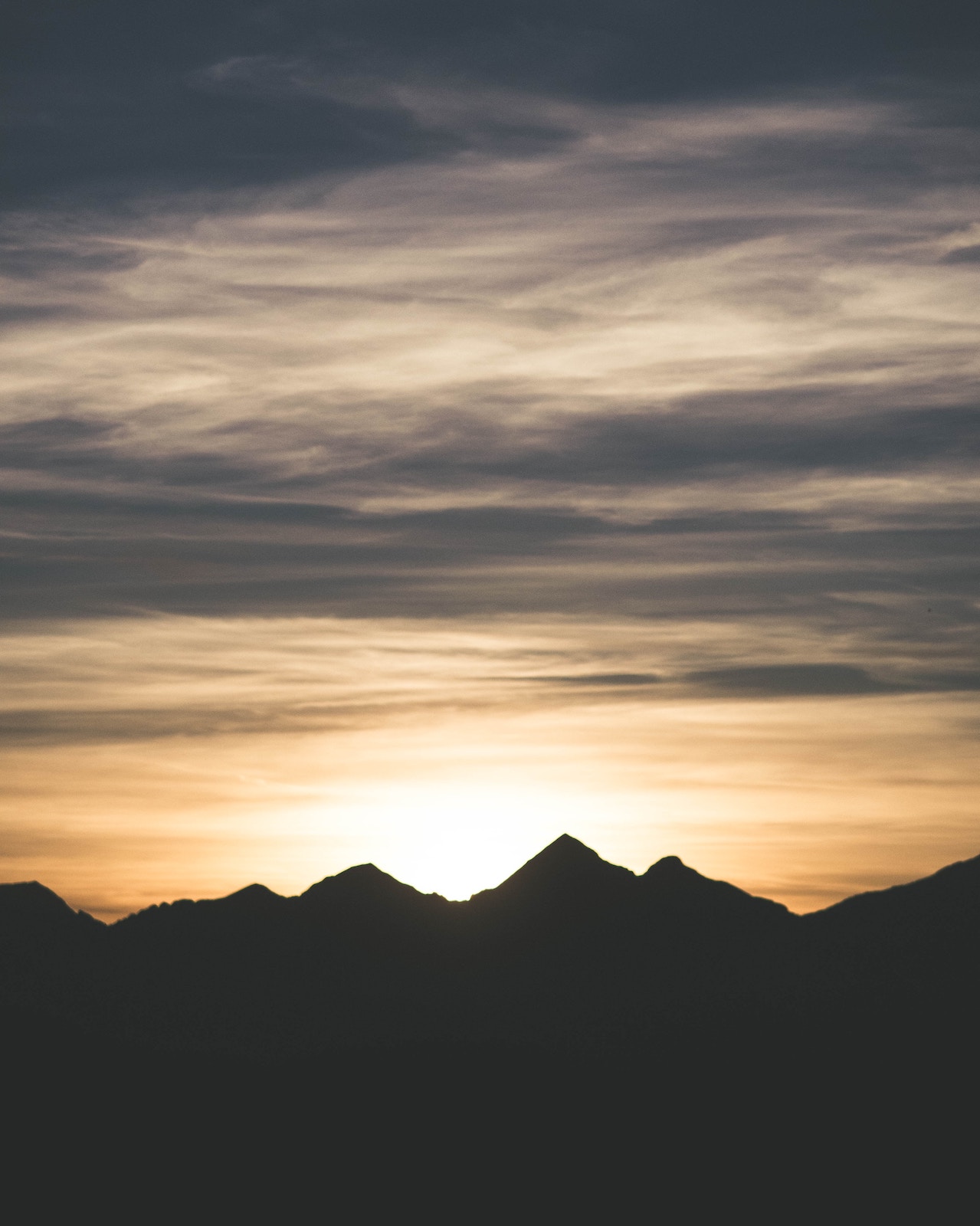 Sunset just over silhouetted mountains. The sky is rich with indigo and pale orange.