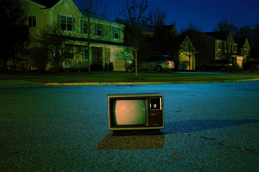 CRT Television sitting on a road in a neighborhood at night.