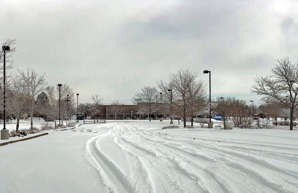 Parking lot in commercial space with unplowed snow and tire tracks.