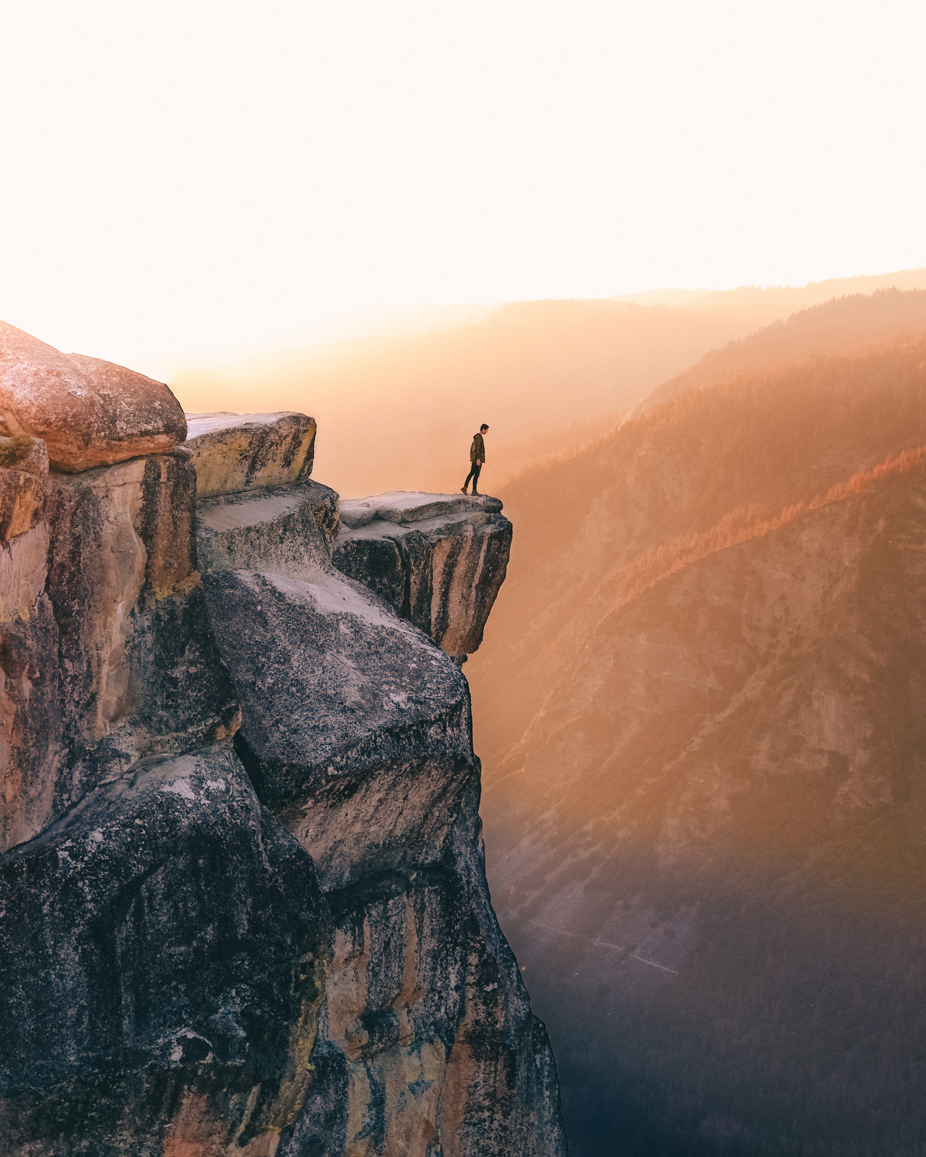 Person stands on a cliff, overlooking a chasm at sunrise.