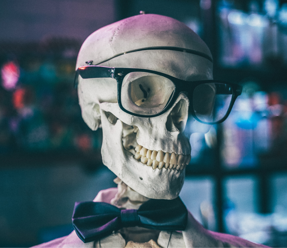 A skeleton in a colorful lab wearing glasses and a bowtie.